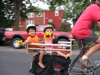 Two children ride on the back of an Xtracycle while holding sunflowers
